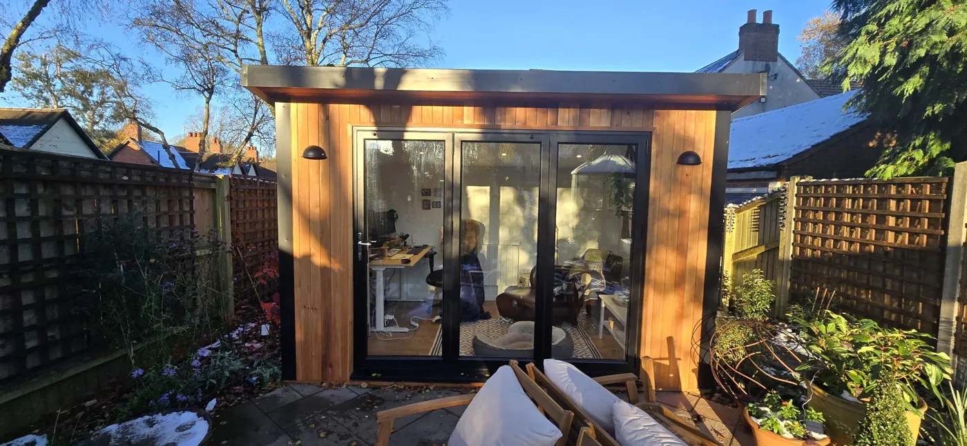 Cedar-clad garden office with bi-fold doors on a Birmingham patio, with snow on the neighbouring roof and in the borders