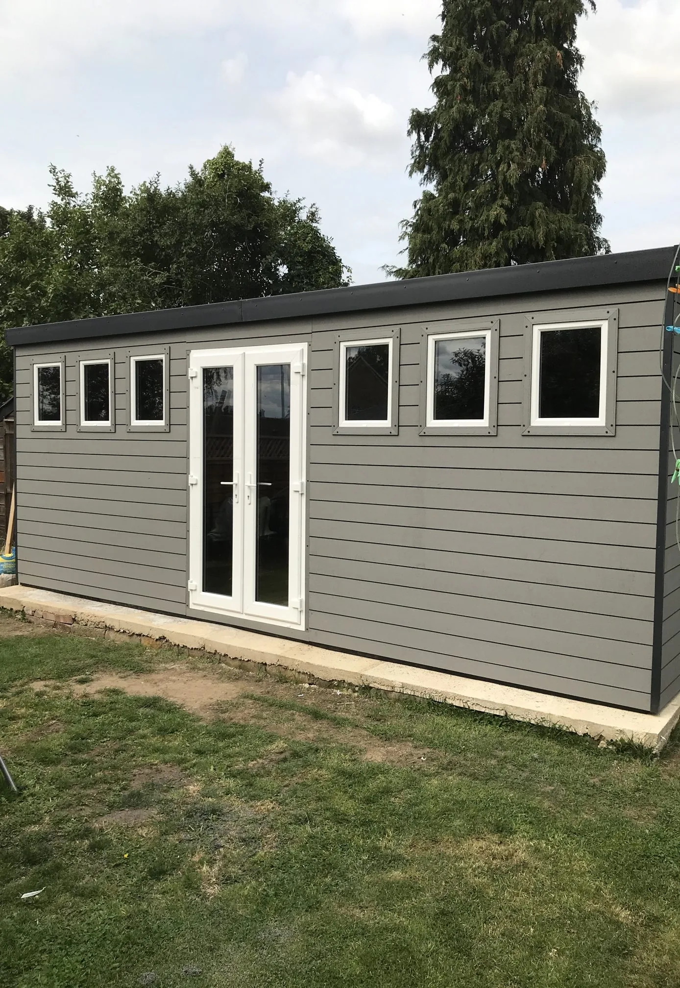 Grey-painted timber workshop with white double doors and a row of windows