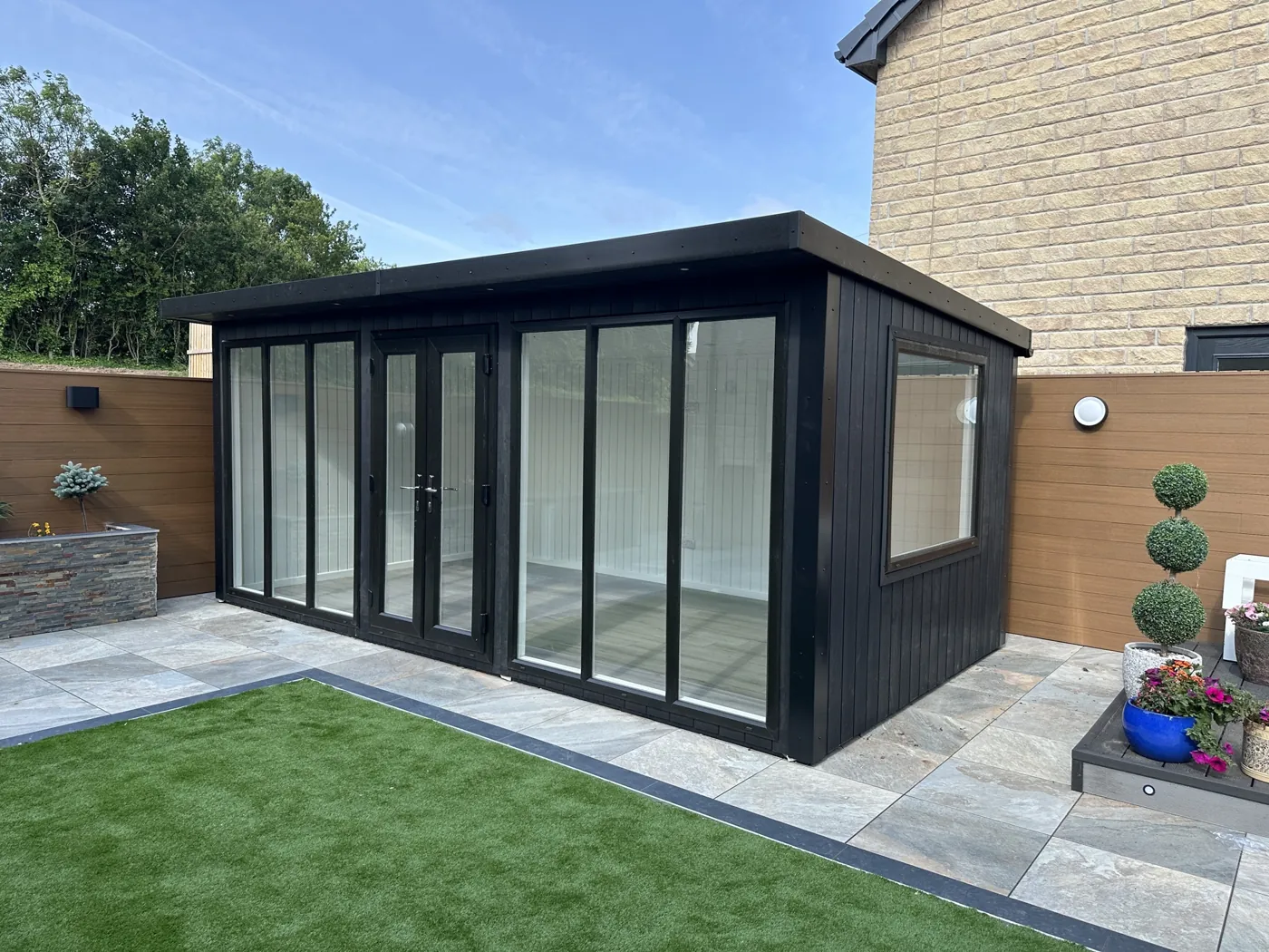 Black composite Chippenham garden room with full-height glazing beside a paved garden
