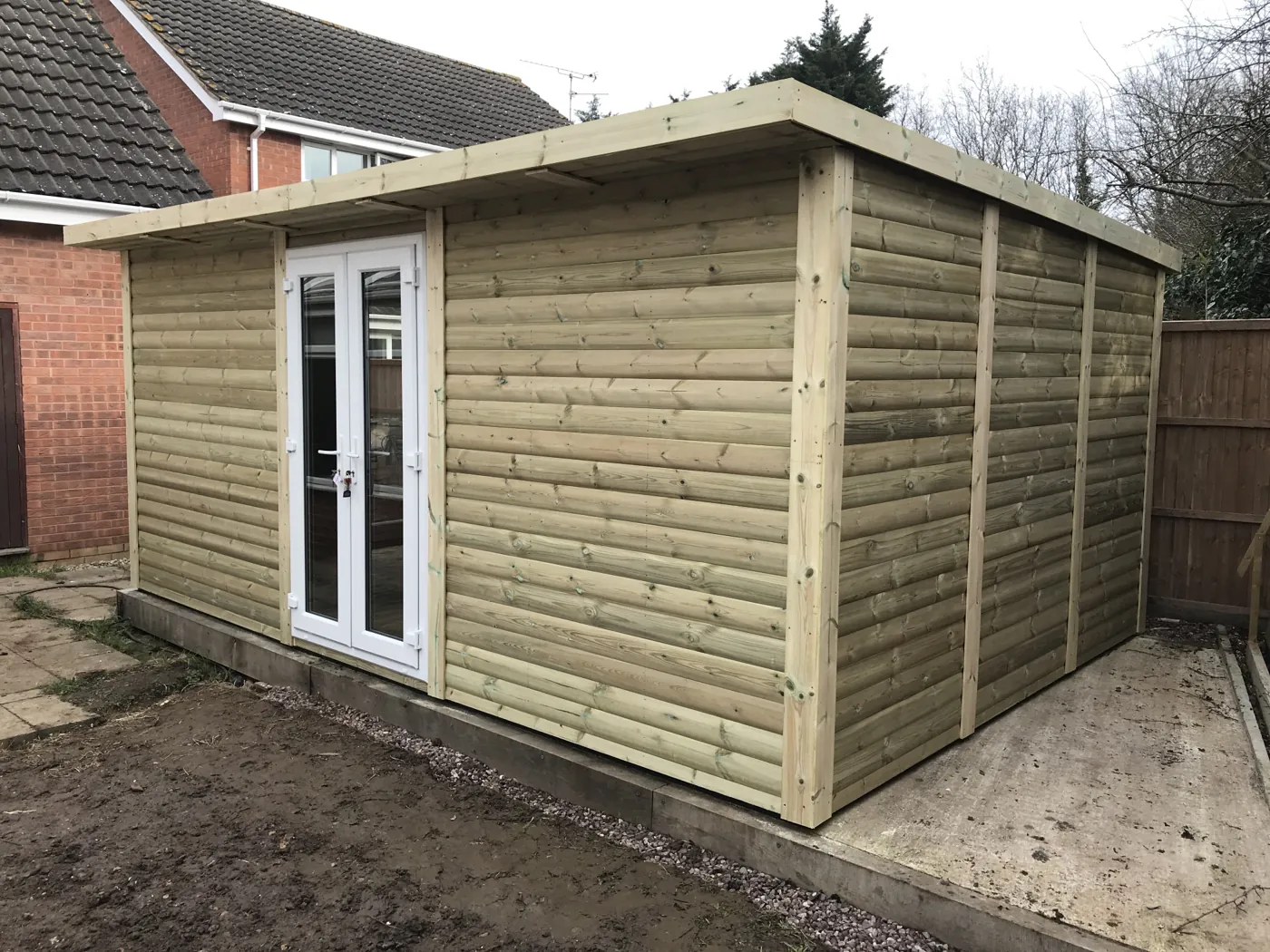 A new garden building clad in pressure-treated timber, with white-framed doors