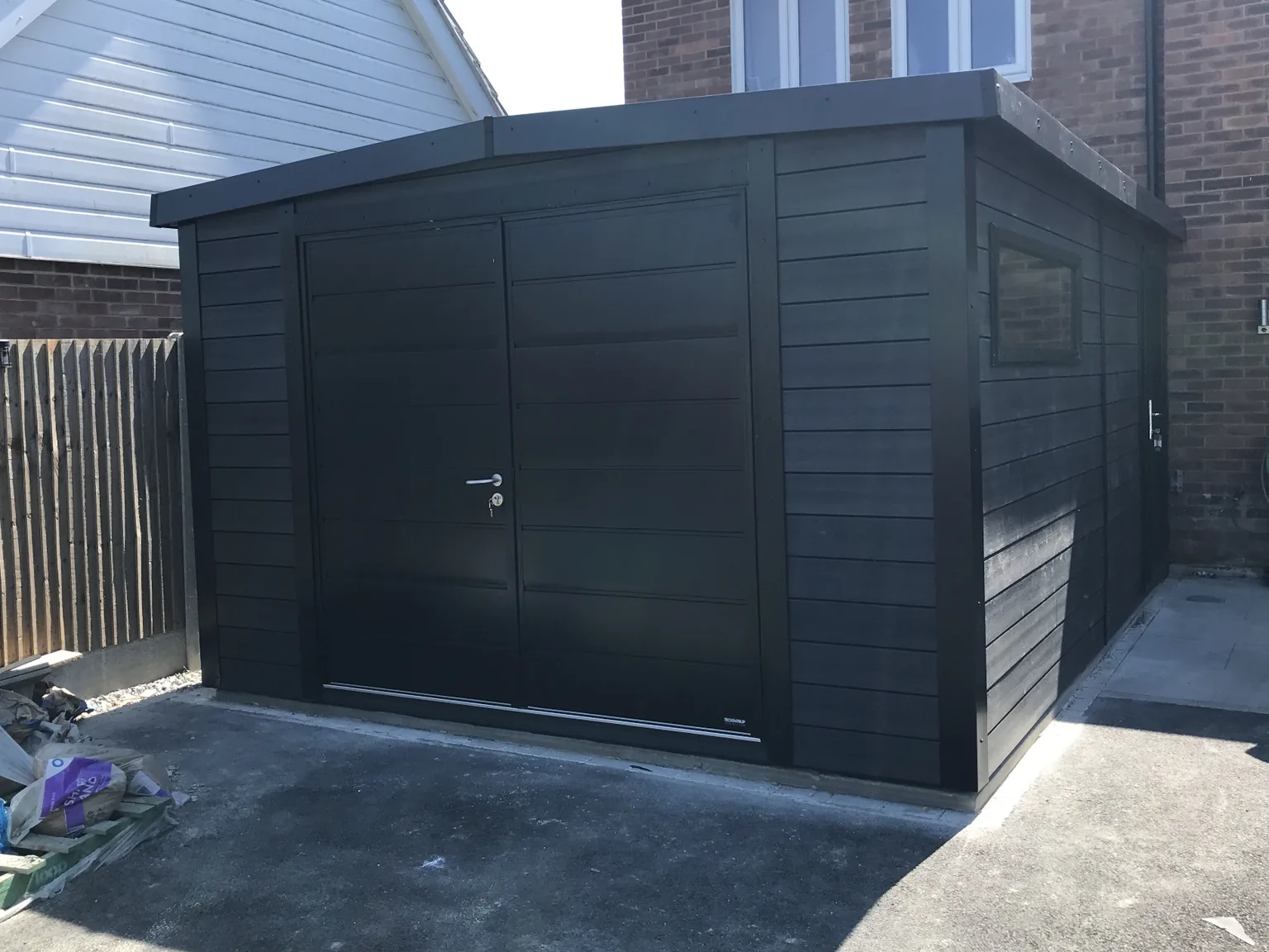 Black composite Noah garage with metal double doors, newly installed on a driveway